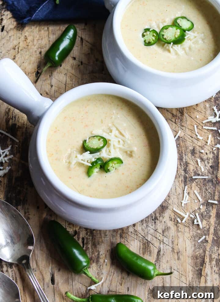 Two bowls of creamy jalapeno popper soup garnished with sliced jalapenos and cheese.