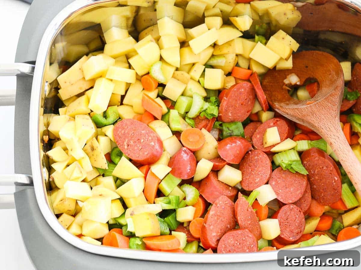 Chopped potato, green bell pepper, and sliced sausage in a slow cooker.