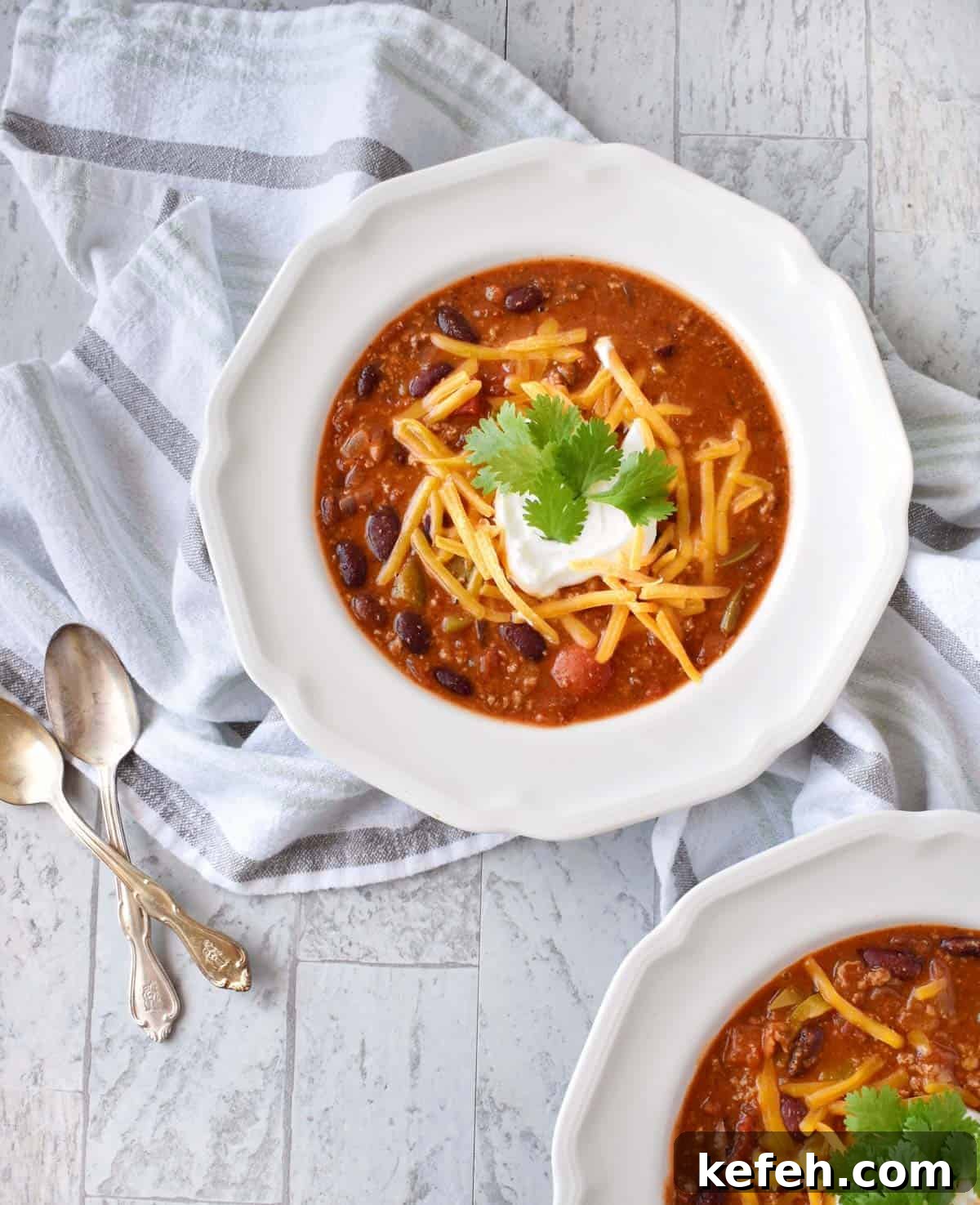 Turkey Taco Chili Soup Recipe — Hearty Weeknight Meal 2 two white bowls with chili and toppings on a striped towel with spoons to the side.