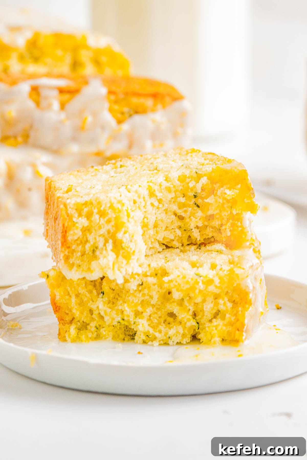 A slice of glazed lemon zucchini bread split in half on a plate. 