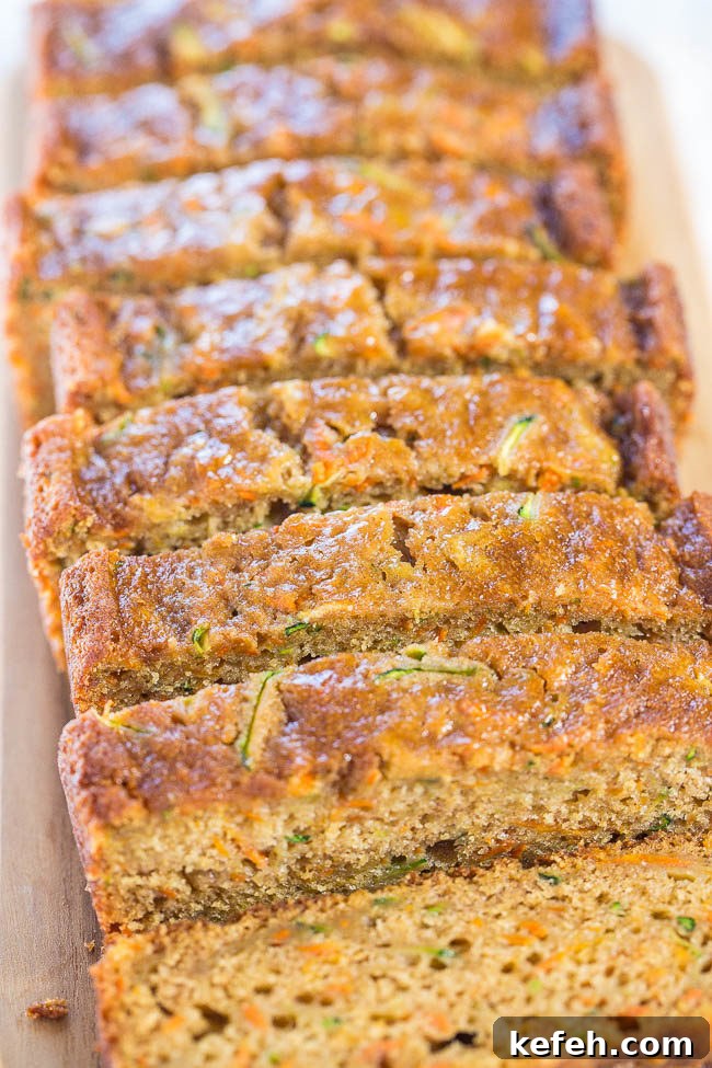 A loaf of zucchini carrot bread sliced on a wooden cutting board. 