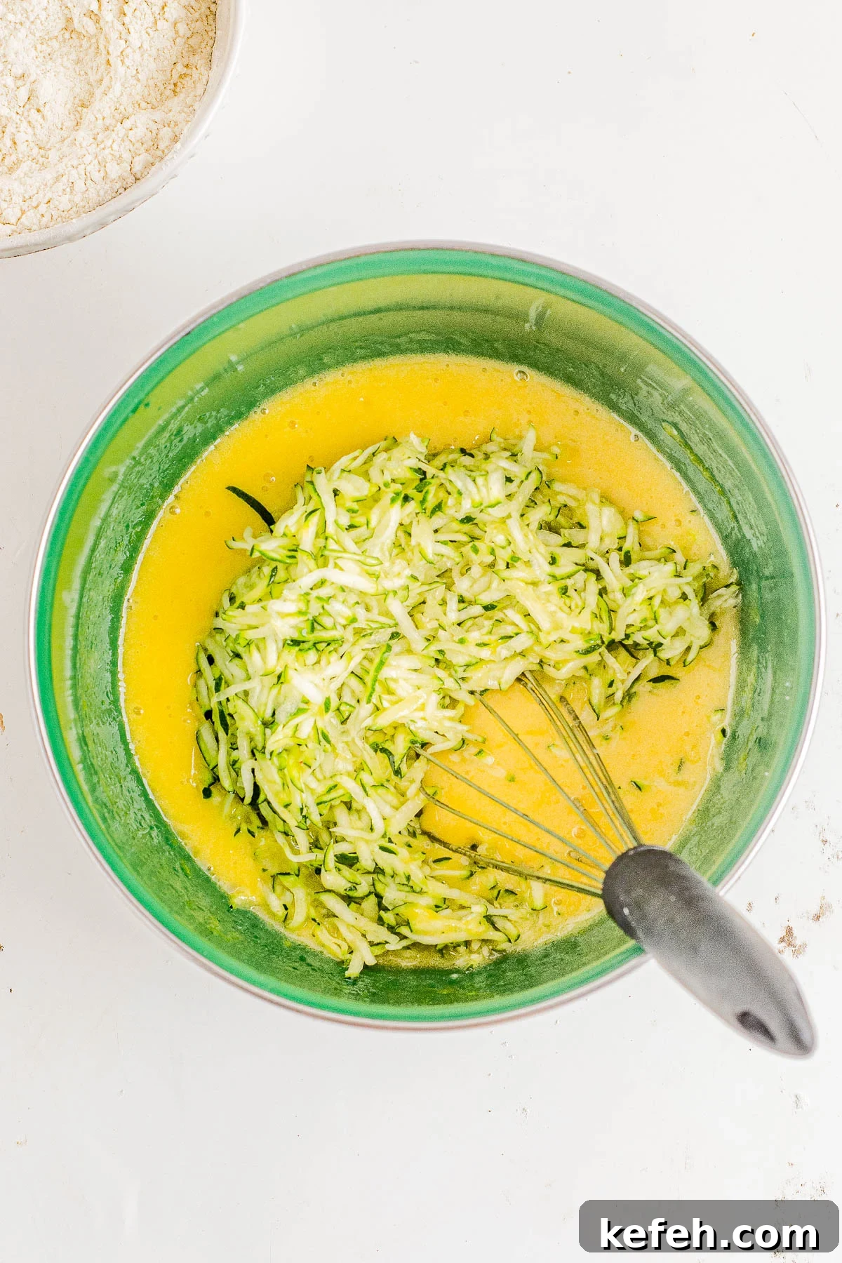 Shredded zucchini being folded into bread batter in a bowl. 