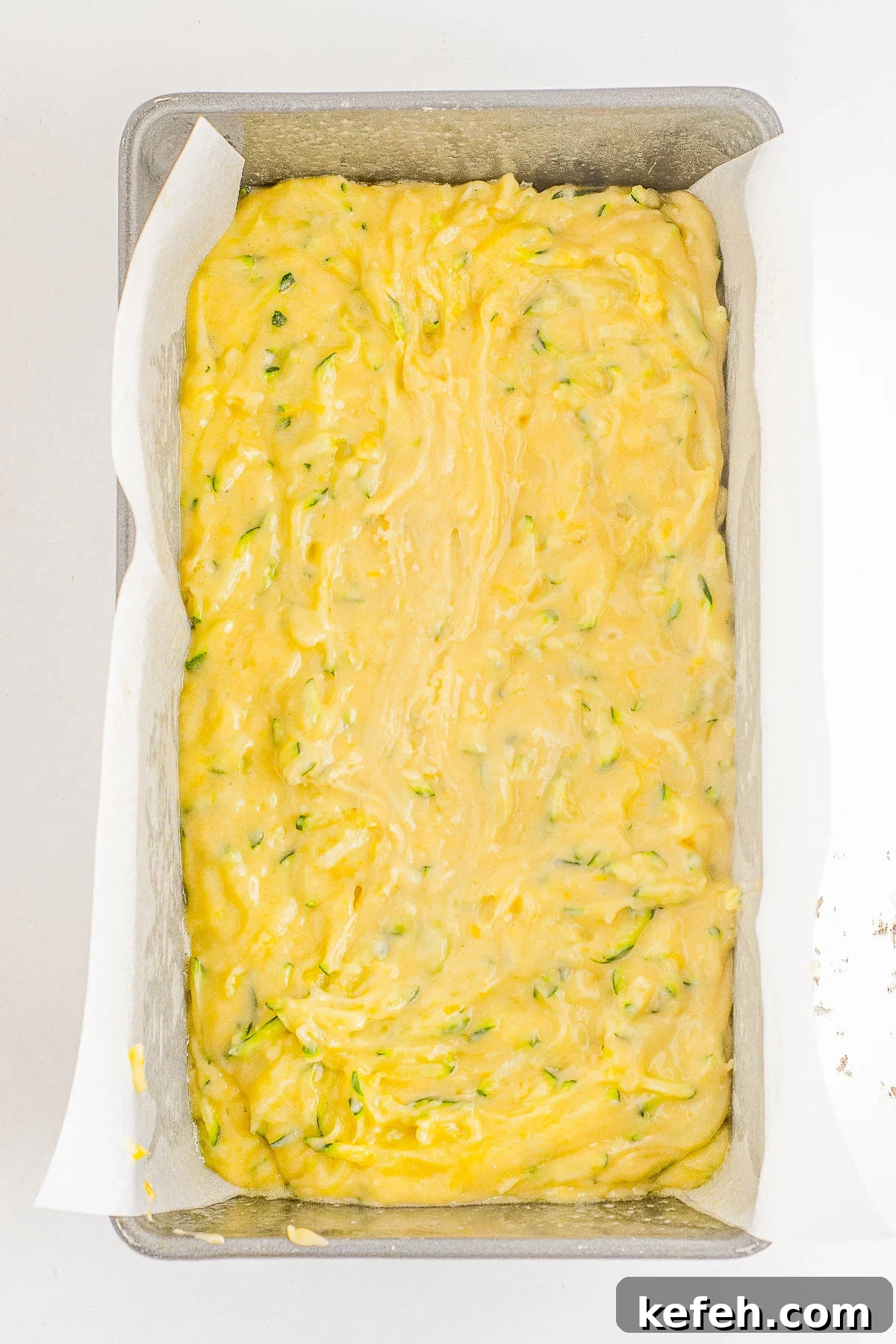 Lemon zucchini bread batter in a parchment paper lined loaf pan. 