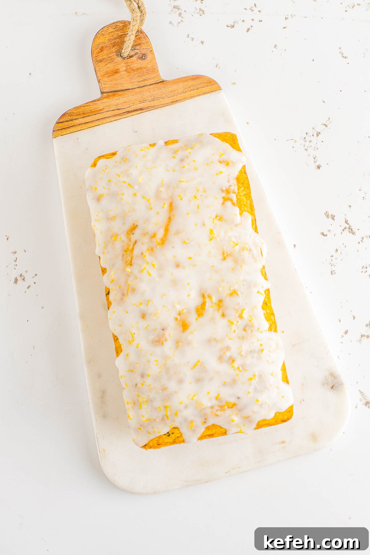 A glazed lemon zucchini bread loaf on a cutting board. 
