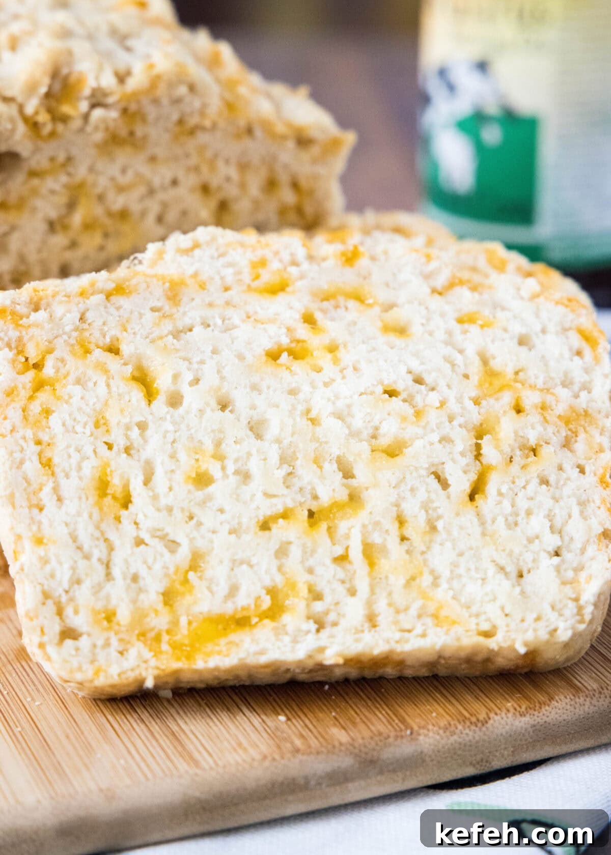 This easy cheddar beer bread recipe is moist, soft, full of beer and cheese flavors, and so quick and easy to make at home. Close up of a slice of beer bread with a loaf in the background