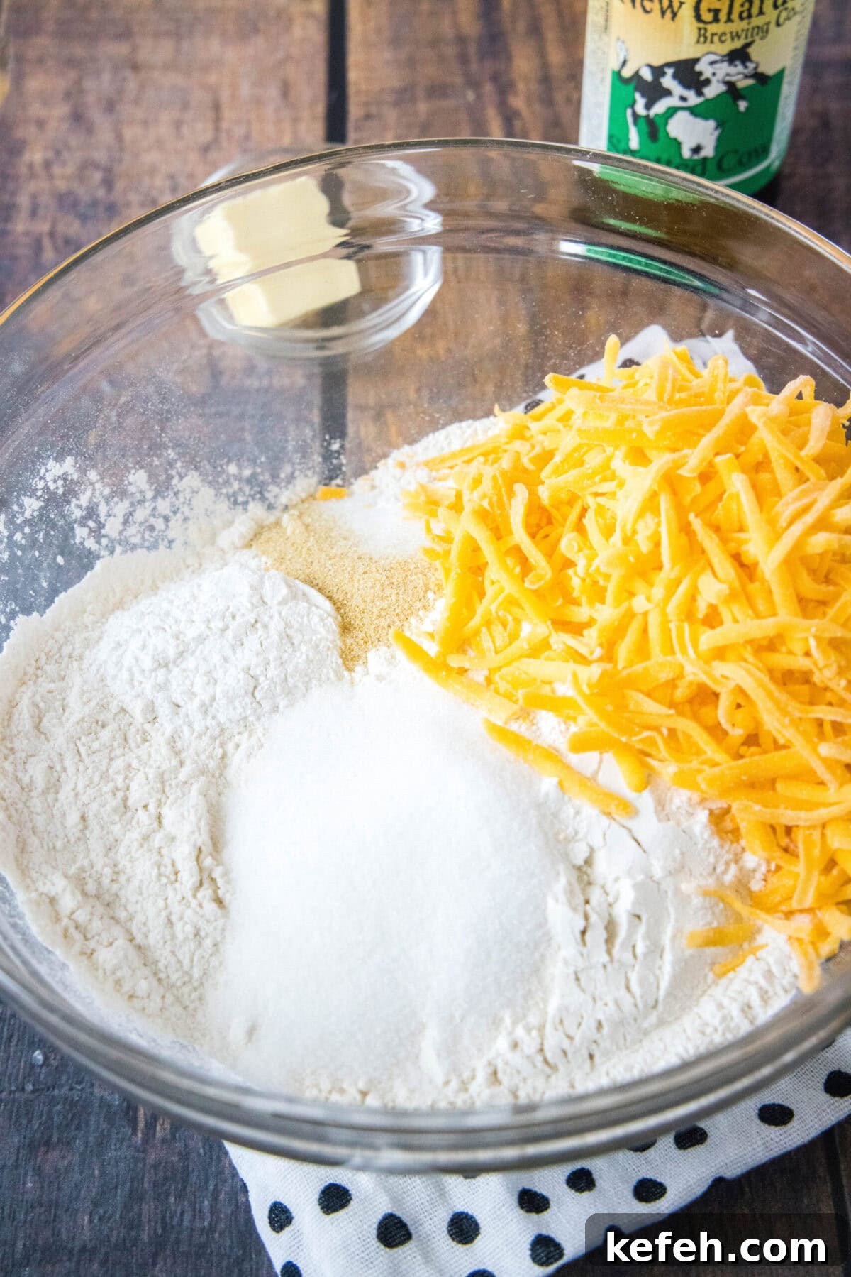 This easy cheddar beer bread recipe is moist, soft, full of beer and cheese flavors, and so quick and easy to make at home. A mixing bowl filled with flour, cheese, salt, sugar, baking powder, and garlic powder