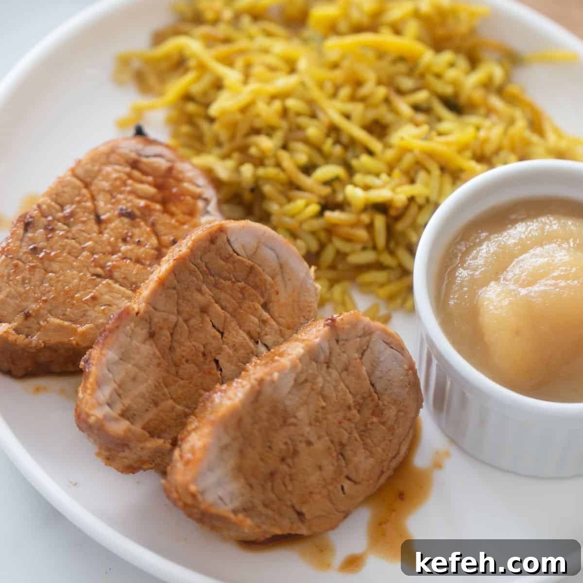 Crispy Air Fryer Pork Tenderloin with Garlic Herb Rub 2 Plate with sliced air fryer pork tenderloin drizzled with juice, a side of homemade applesauce, and rice pilaf.