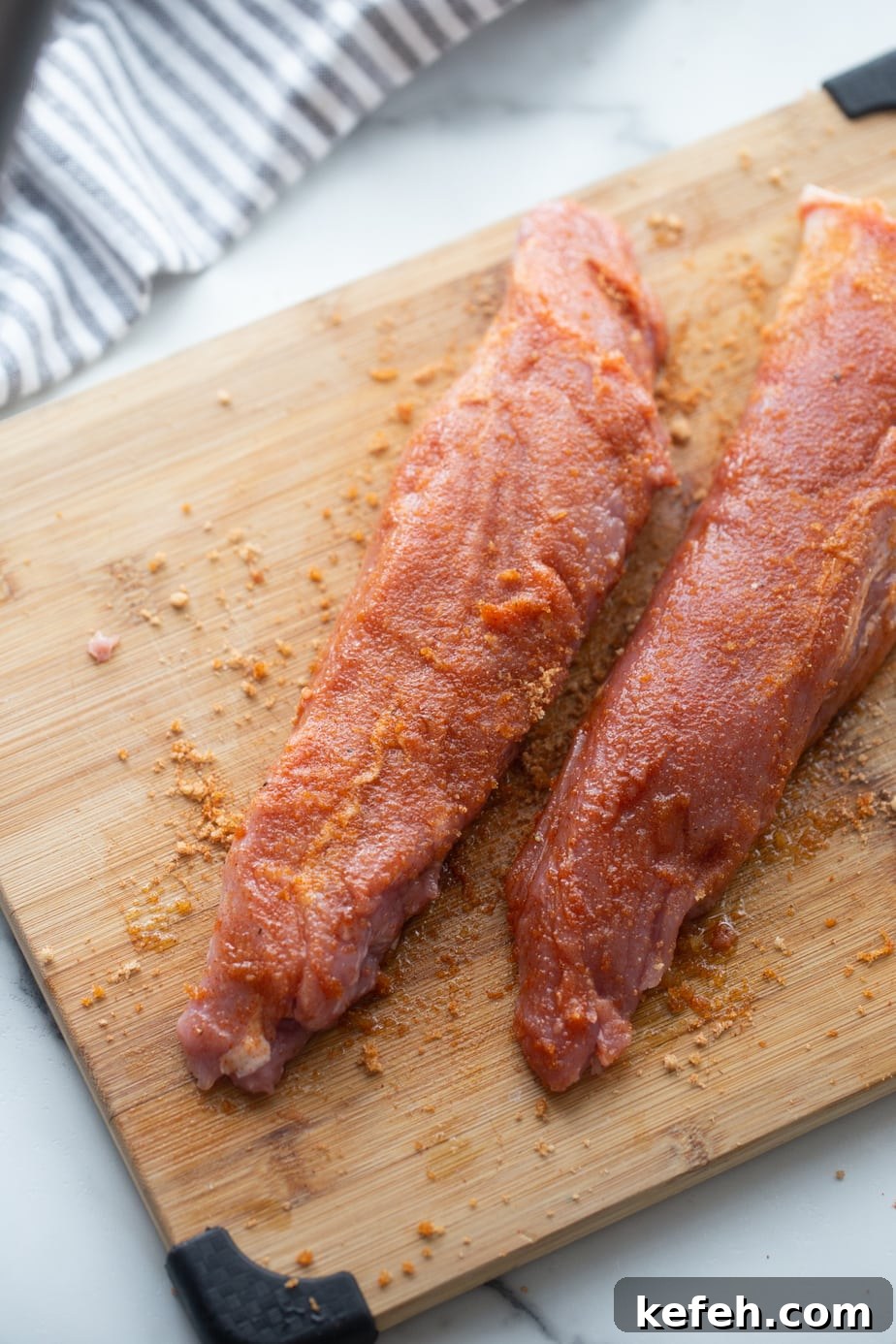 Crispy Air Fryer Pork Tenderloin with Garlic Herb Rub 7 Two raw pork tenderloins on a wooden cutting board coated with spice rub.
