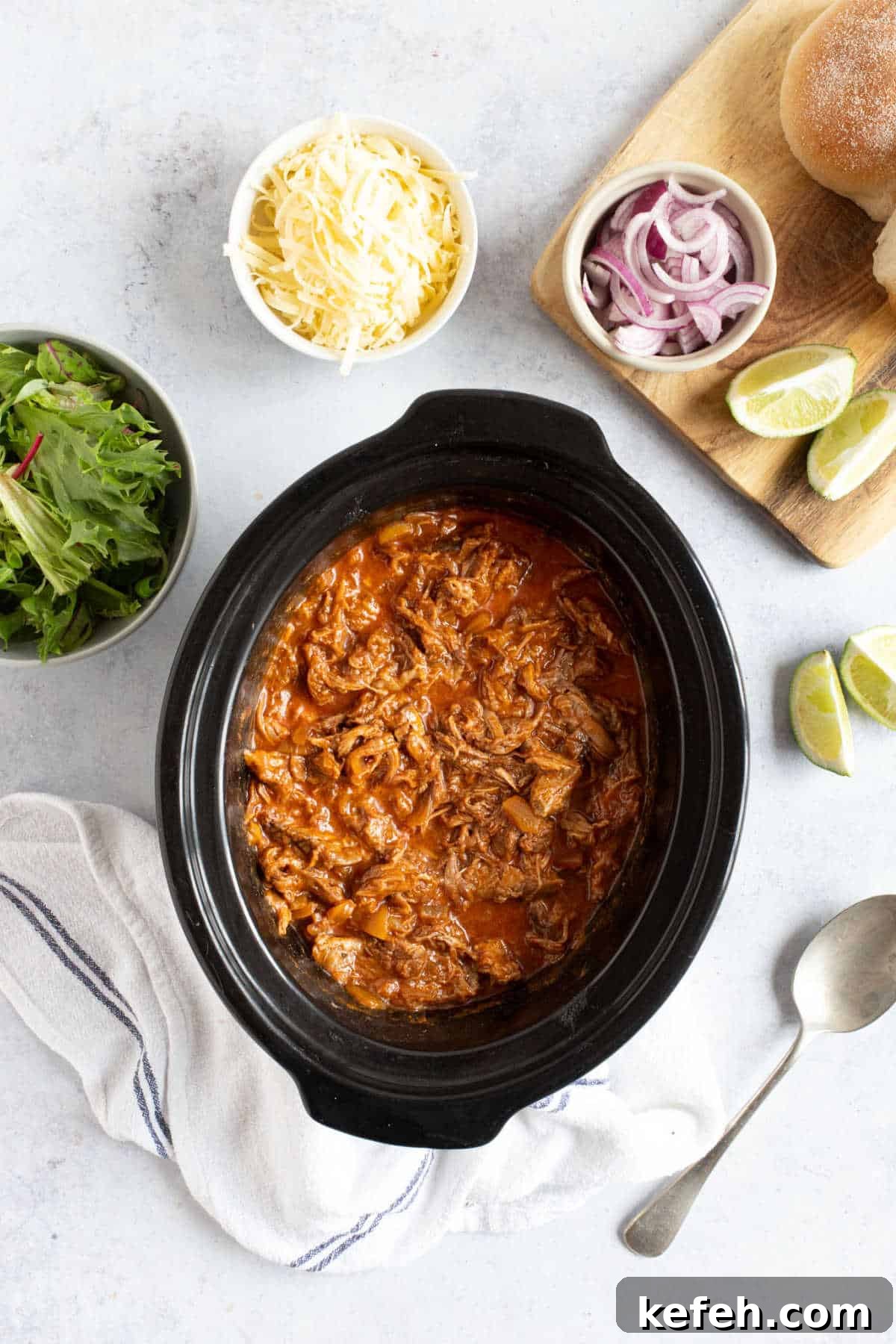 Slow Cooker Pulled Beef Recipe for Tender, Shredded Meat 5 Pulled beef in a slow cooker with grated cheese, lime wedges and red onion.