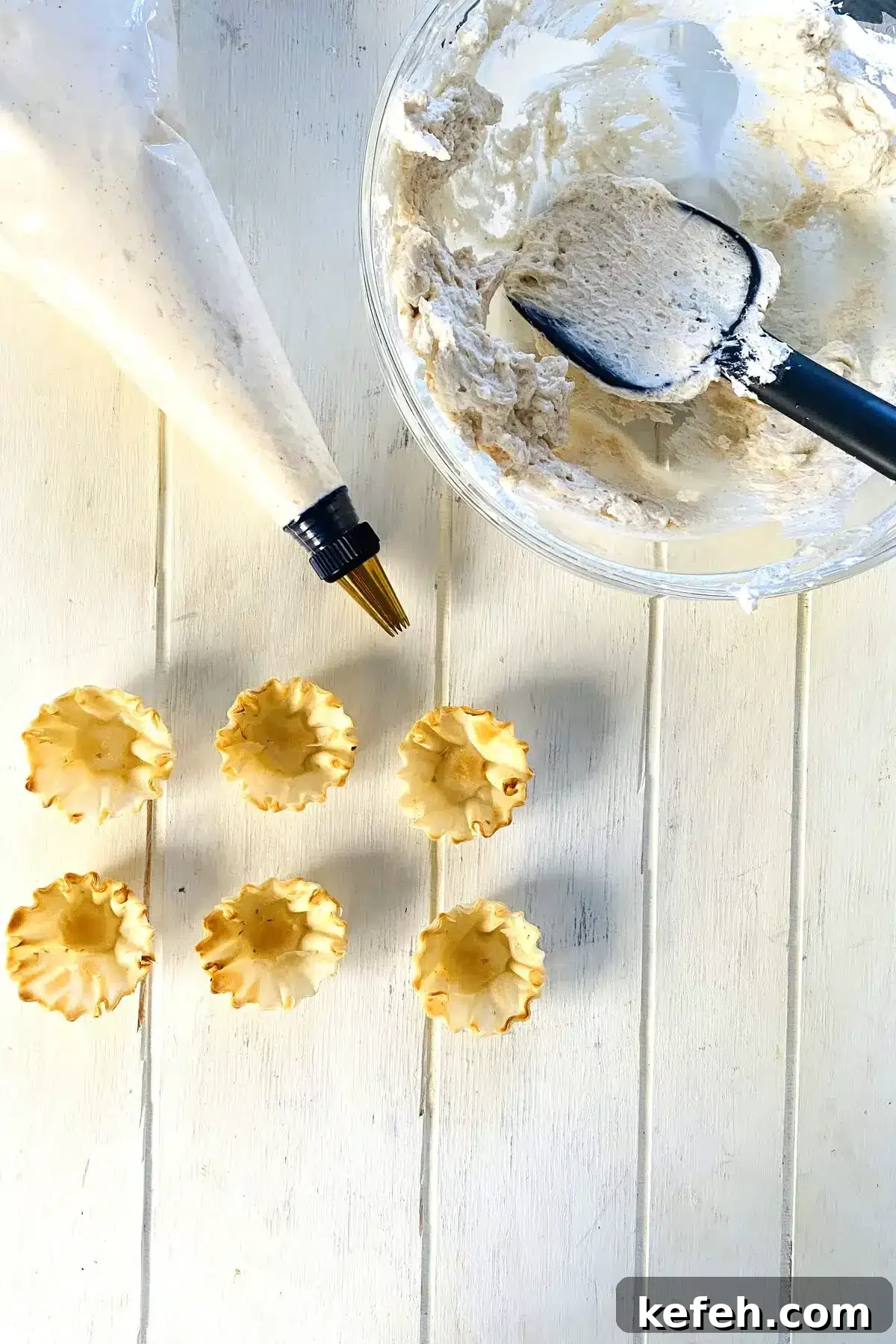 Mini No-Bake Philadelphia Cheesecakes Recipe 8 Piping bag filled with cheesecake filling and empty phyllo cups.