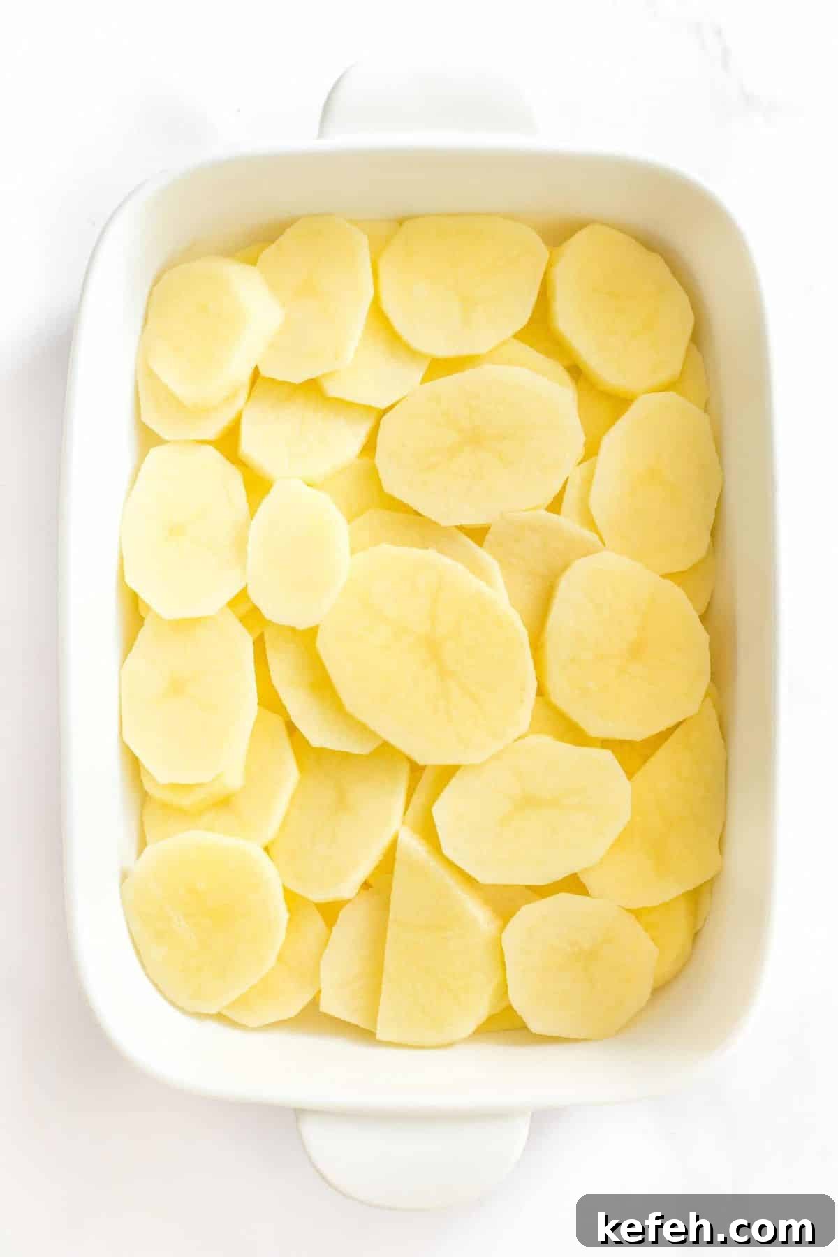 Creamy Gluten-Free Scalloped Potatoes (Dairy-Free, Vegan) Sliced potato rounds in casserole dish.