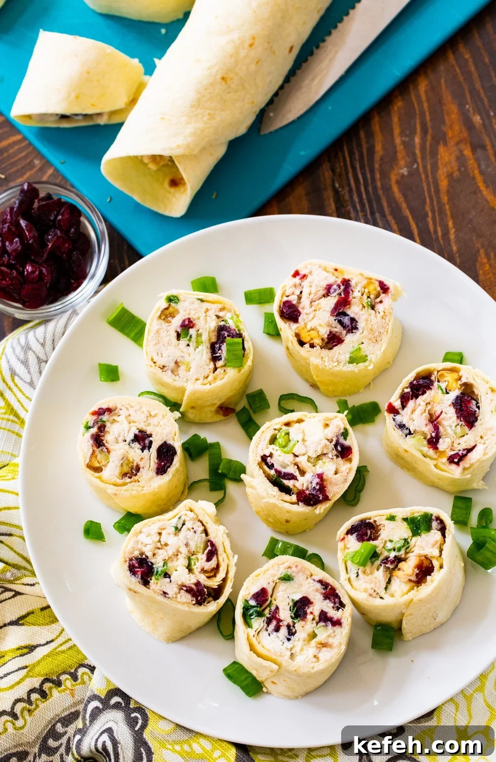 Bite-Sized Chicken Cranberry Pinwheels 3 Cut pinwheels on a plate with uncut tortilla rolls on a cutting board.