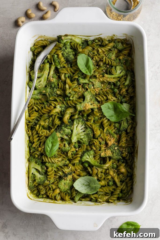 Baked Green Pesto Pasta Casserole Recipe 2 Green Pesto Pasta Casserole in casserole dish topped with basil and vegan parmesan with serving spoon