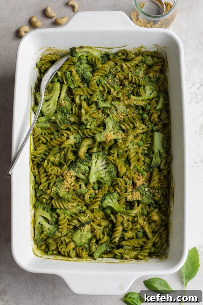 Baked Green Pesto Pasta Casserole Recipe 6 Green Pesto Pasta Casserole in casserole dish topped with basil and vegan parmesan with serving spoon