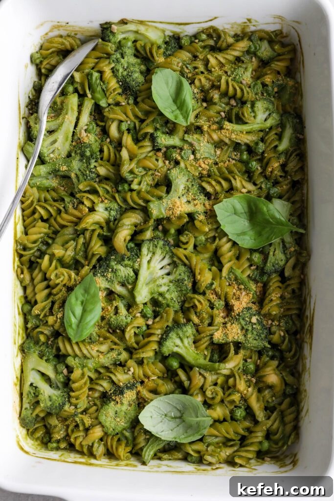 Baked Green Pesto Pasta Casserole Recipe 7 Green Pesto Pasta Casserole in casserole dish topped with basil and vegan parmesan with serving spoon