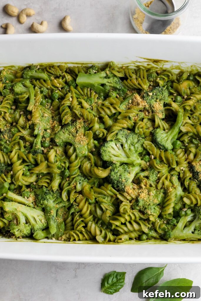 Baked Green Pesto Pasta Casserole Recipe 8 Green Pesto Pasta Casserole in casserole dish topped with basil and vegan parmesan with serving spoon