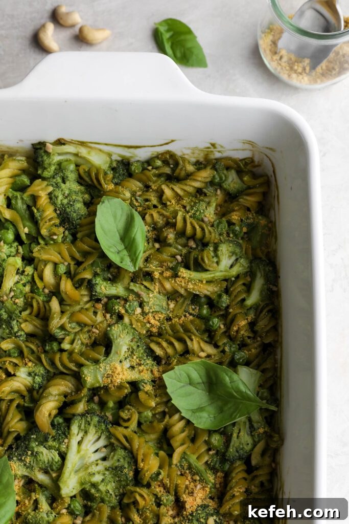 Baked Green Pesto Pasta Casserole Recipe 9 Green Pesto Pasta Casserole in casserole dish topped with basil and vegan parmesan with serving spoon
