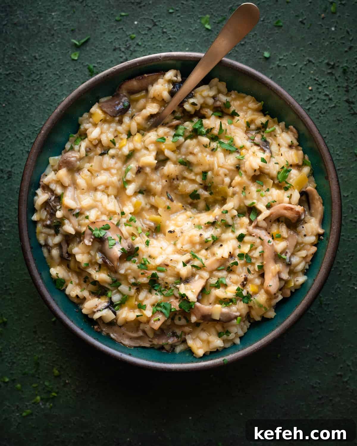 Vegan Holiday Survival Guide: Thrive at Festive Meals 16 creamy, velvety vegan mushroom risotto in a green bowl with spoon dug in on a dark green table.