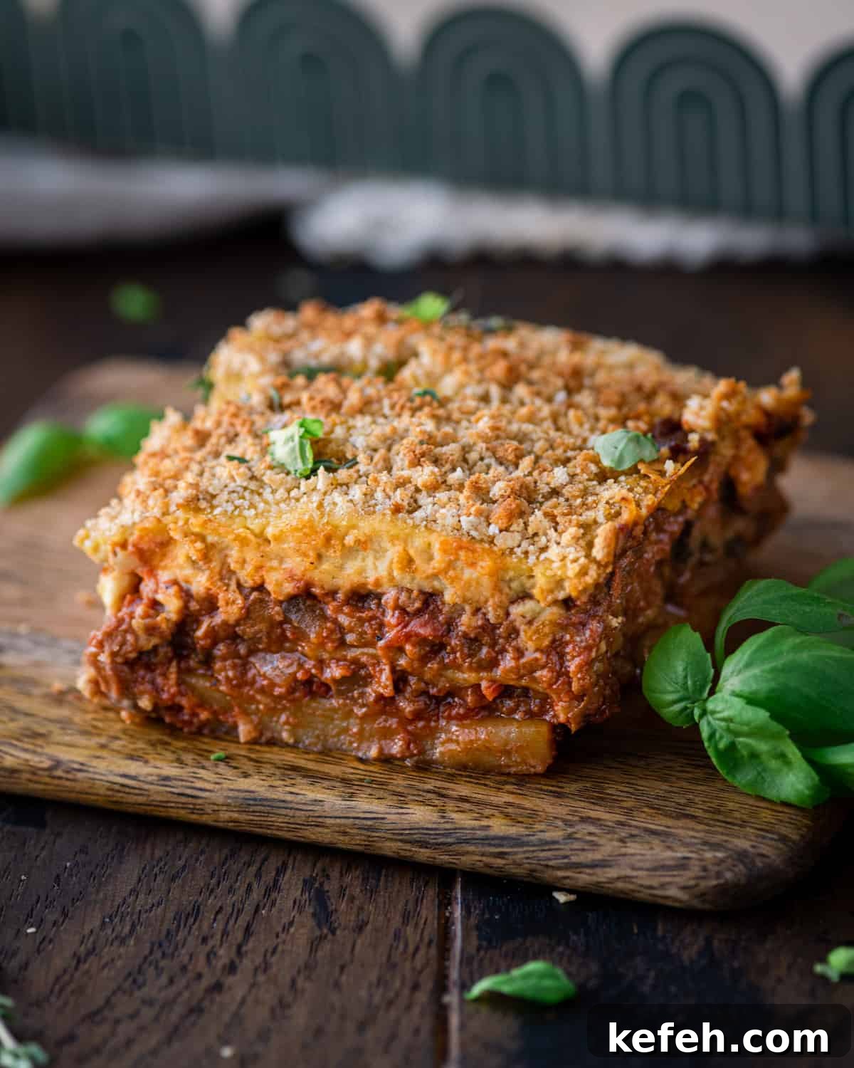 Vegan Holiday Survival Guide: Thrive at Festive Meals 4 slice of vegan moussaka on a small wooden cutting board with fresh basil on the side.