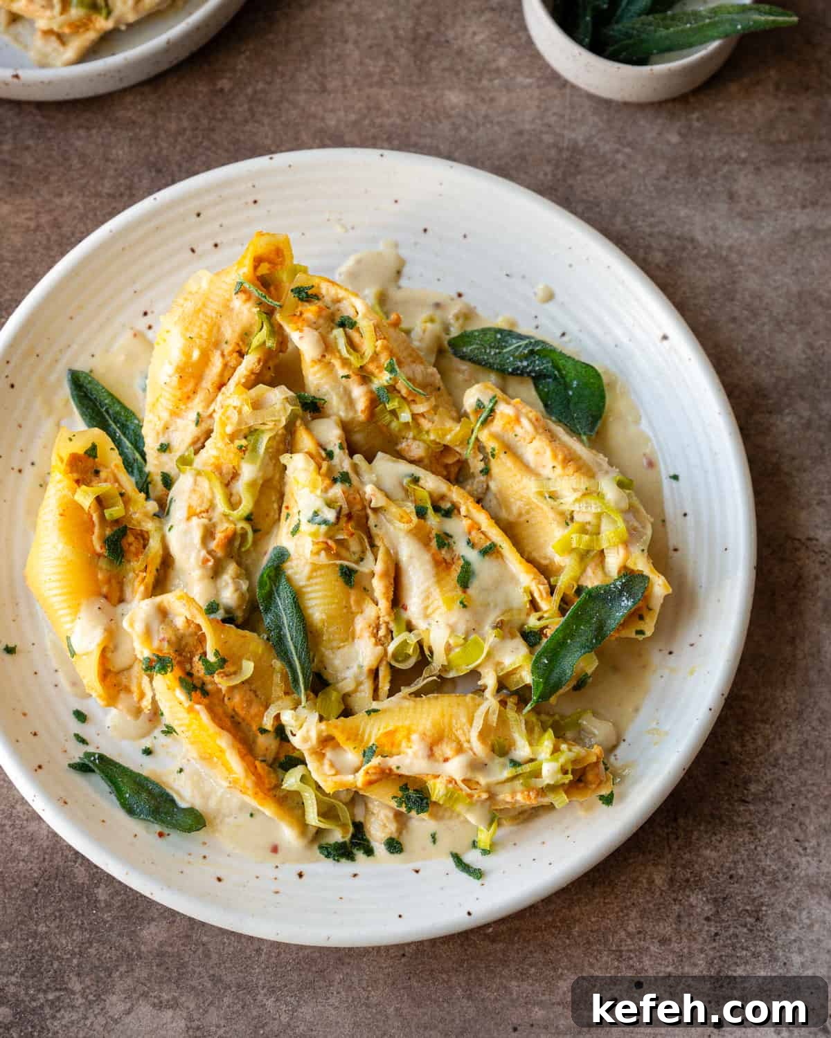 Vegan Holiday Survival Guide: Thrive at Festive Meals 5 pumpkin ricotta stuffed jumbo shells on a speckled white plate, garnished with cream sauce and fried sage.