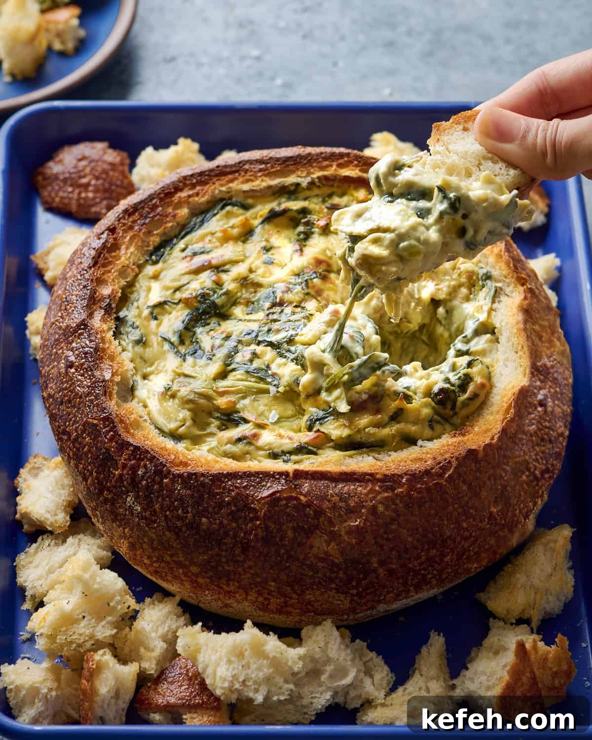 Vegan Holiday Survival Guide: Thrive at Festive Meals 10 Woman dipping bread into spinach artichoke dip in a bread bowl.