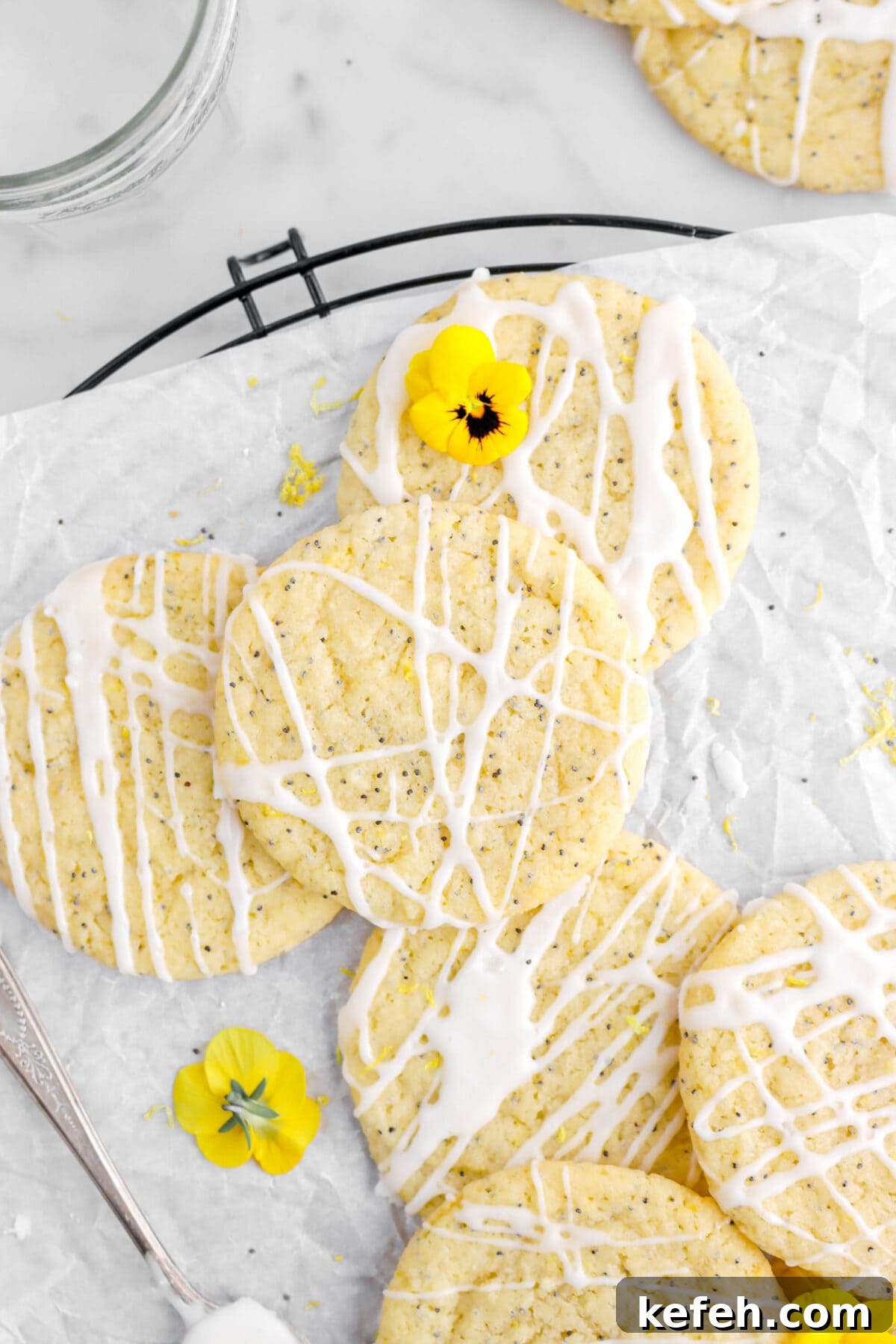 Lemon Poppy Seed Cookies with Lemon Drizzle Recipe 3 overhead close up of lemon poppy seed cookies piled on top of each other on parchment paper with yellow flowers around.