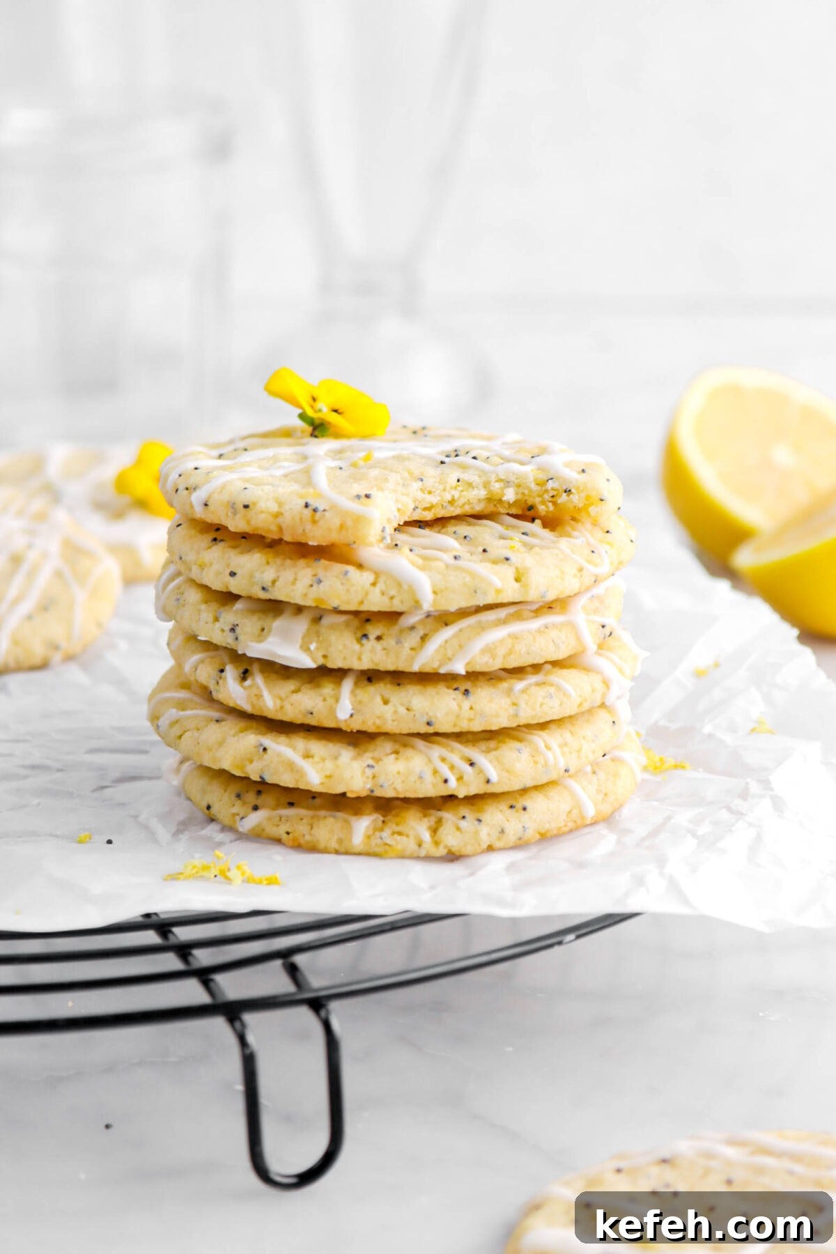 Lemon Poppy Seed Cookies with Lemon Drizzle Recipe 4 six stacked lemon poppy seed cookies with top cookie missing a bite on a black cooling rack with parchment paper.