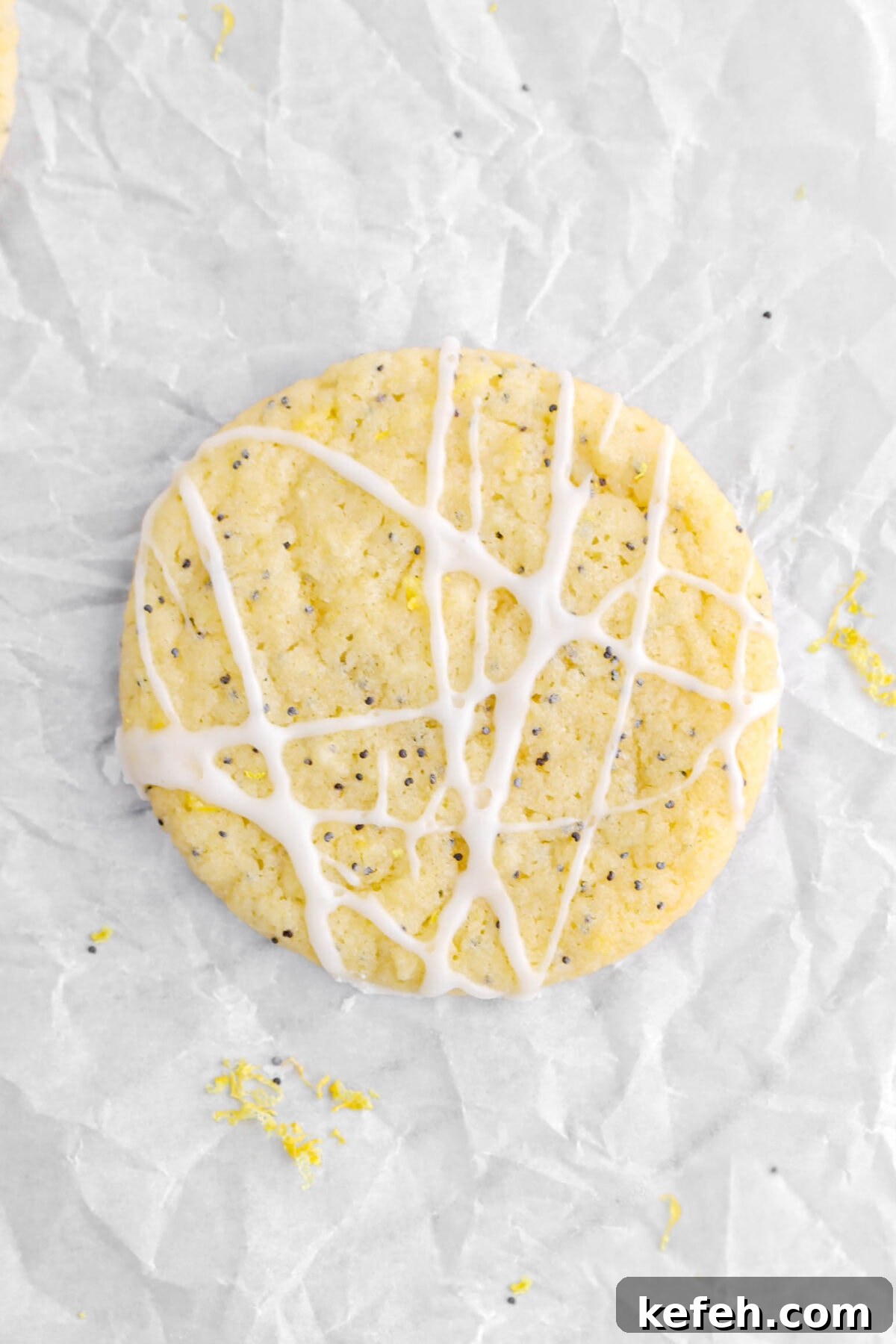 Lemon Poppy Seed Cookies with Lemon Drizzle Recipe 5 overhead close up of iced lemon poppy seed cookie on parchment paper with lemon zest around.