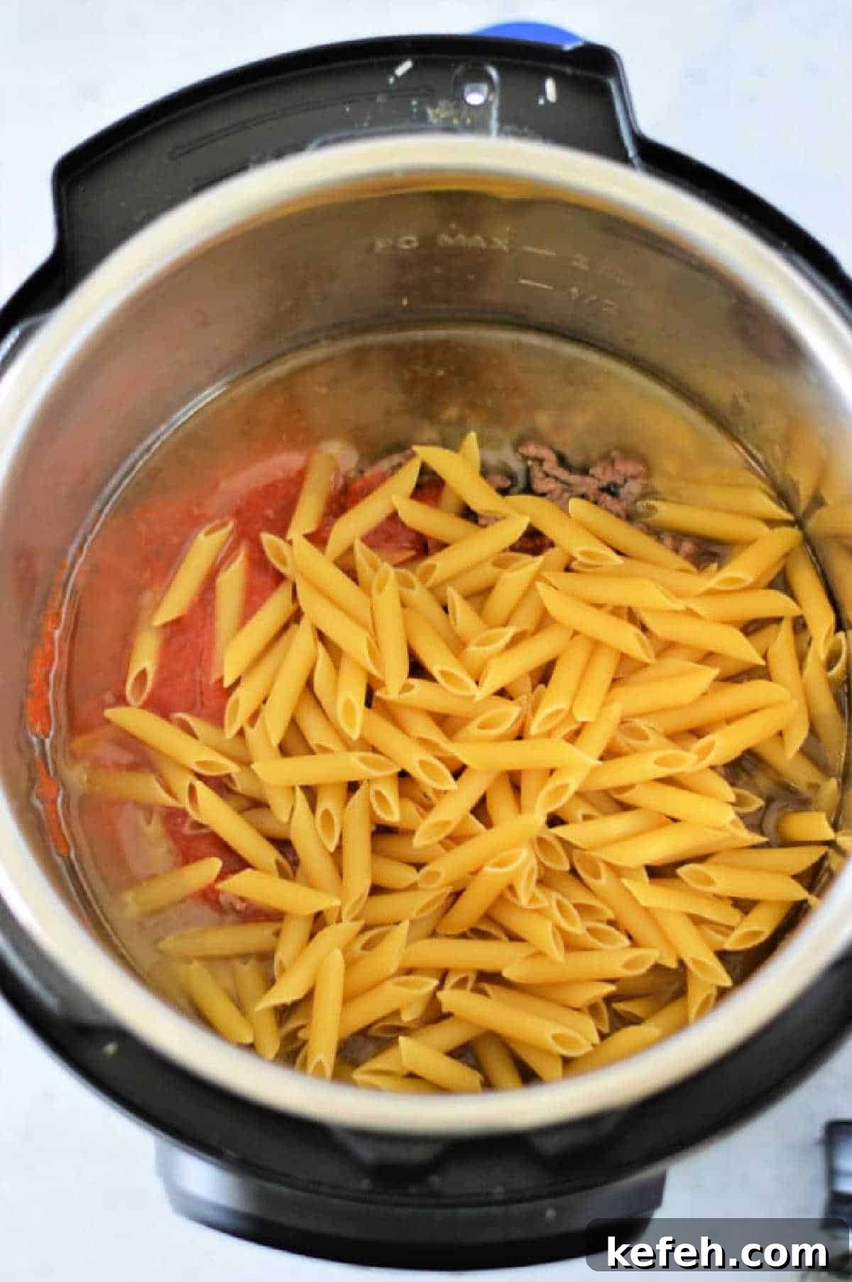 Creamy Instant Pot Penne Pasta Recipe 4 Uncooked instant pot penne pasta, ground meat, and tomato sauce are combined in the Instant Pot, ready to be cooked for a quick and delicious meal.