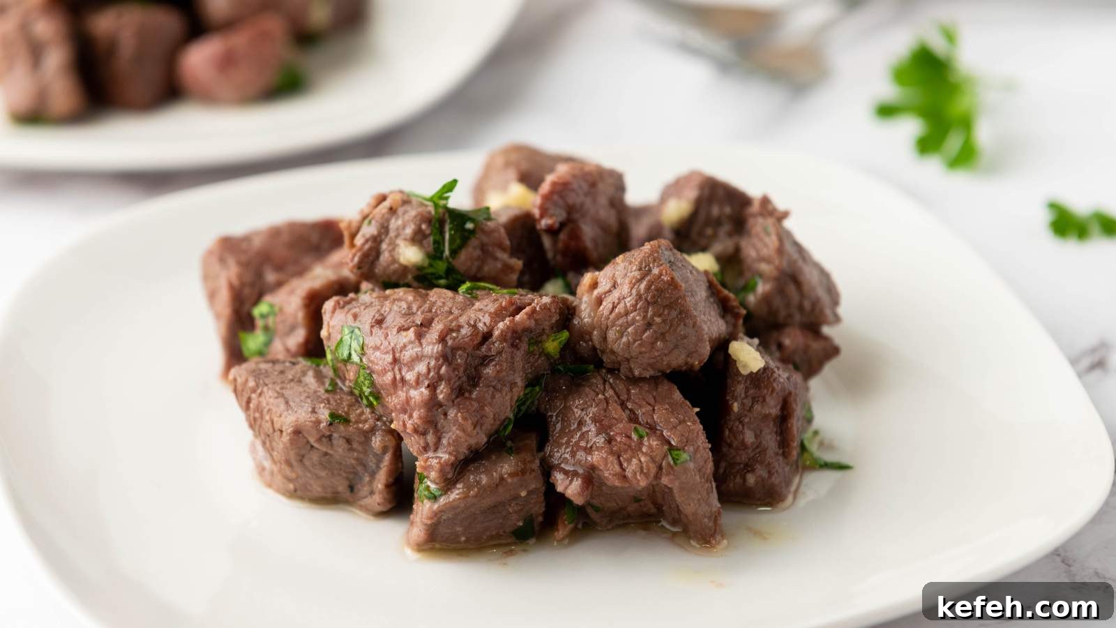 25 Low-Carb Dinners Even Carb Lovers Can't Resist 15 A white plate with cooked steak bites garnished with chopped herbs.