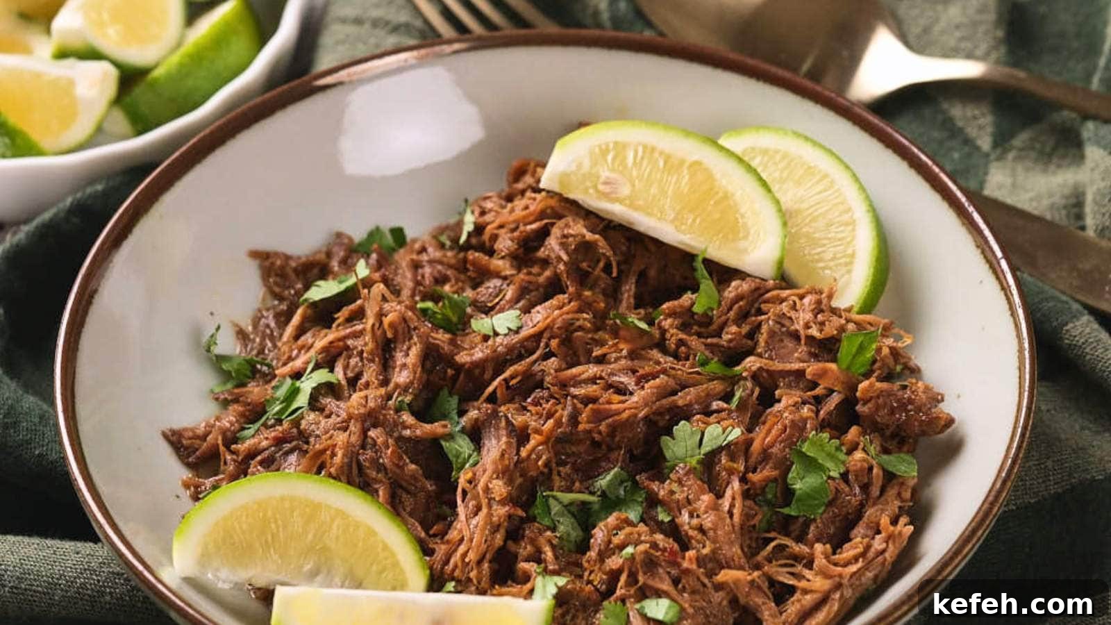 25 Low-Carb Dinners Even Carb Lovers Can't Resist 17 A plate of beef barbacoa garnished with chopped cilantro and lime wedges, placed on a green cloth.