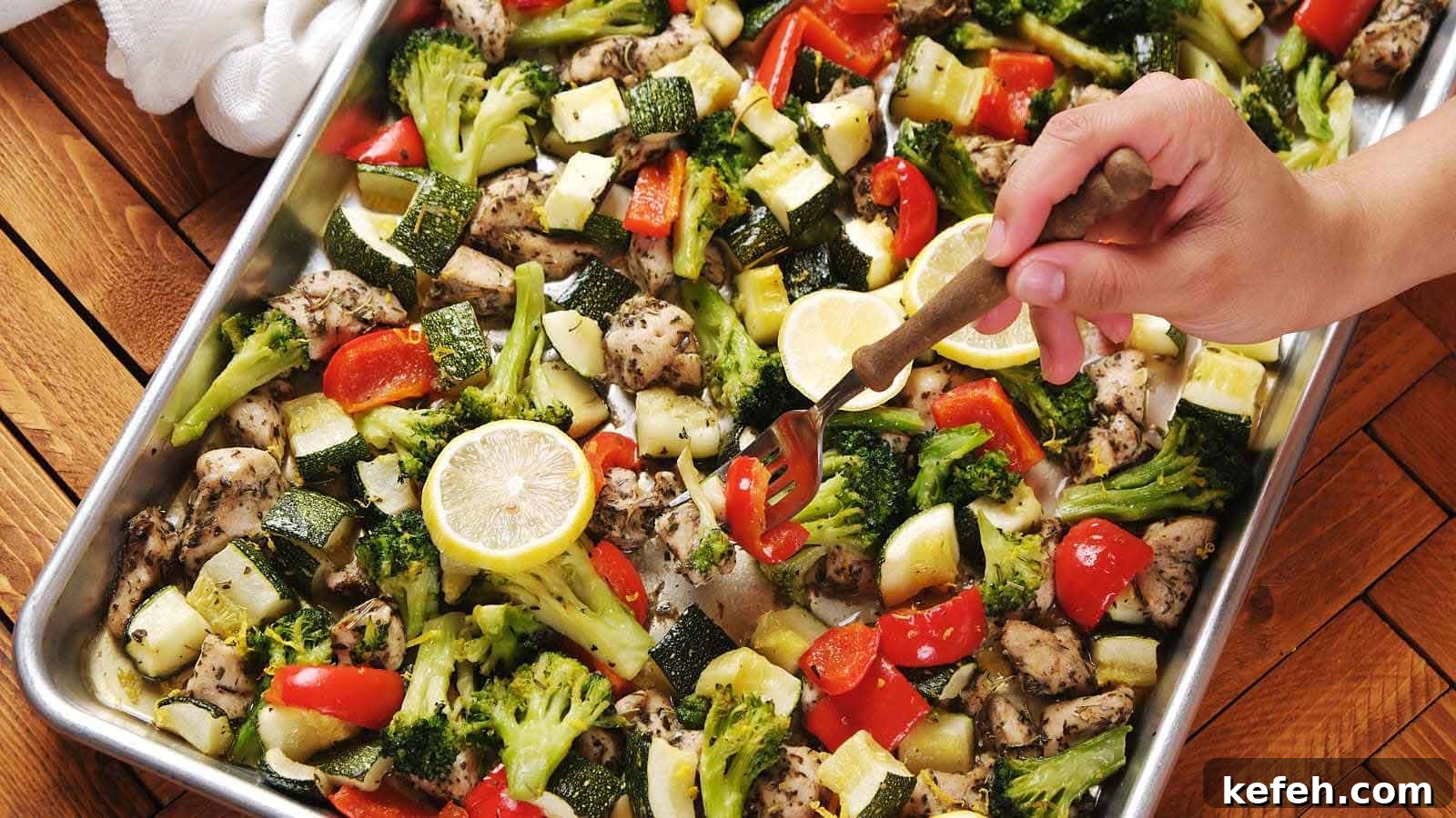 25 Low-Carb Dinners Even Carb Lovers Can't Resist 3 A hand uses a fork to serve a sheet pan meal with baked chicken, broccoli, zucchini, red bell pepper, and lemon slices on a metal tray.