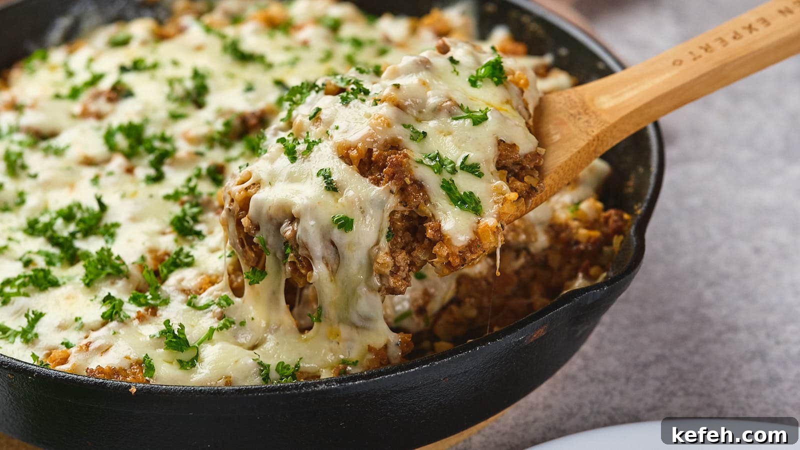 25 Low-Carb Dinners Even Carb Lovers Can't Resist 6 A wooden spoon lifting a serving of italian ground beef skillet garnished with parsley from a cast-iron skillet.