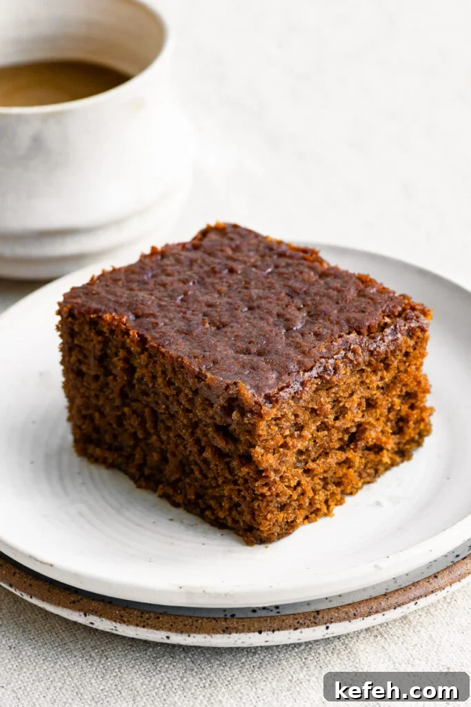 Classic Moist Gingerbread Cake Recipe 2 Slice of gingerbread cake on a plate next to a cup of coffee.