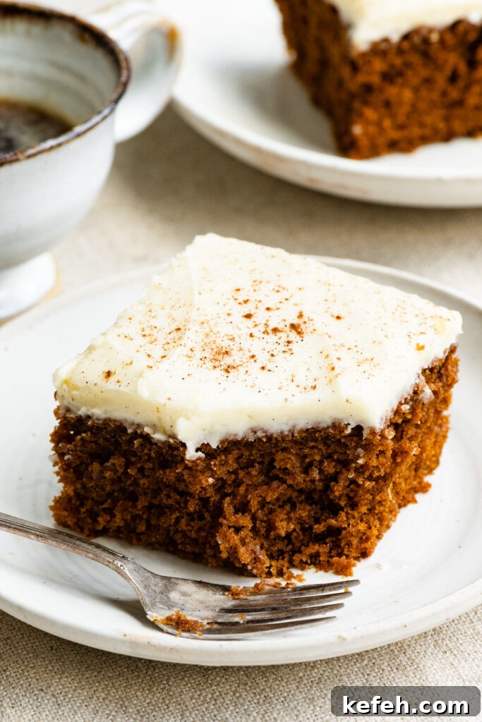 Classic Moist Gingerbread Cake Recipe 13 Slice of gingerbread cake topped with frosting on a plate with a fork and a bite missing out of it