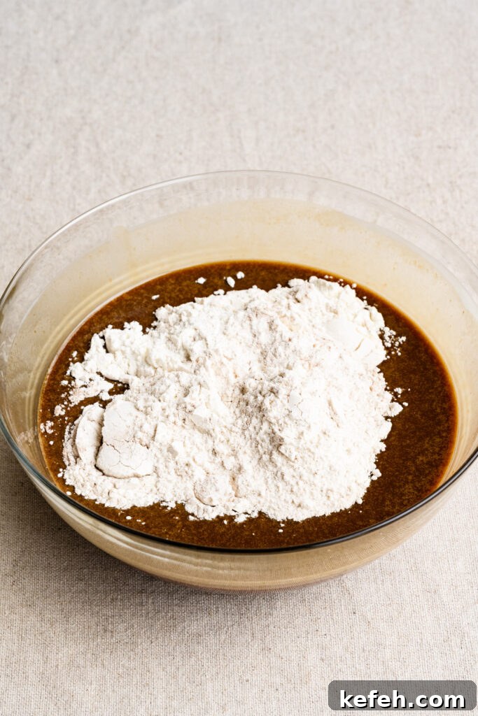 Classic Moist Gingerbread Cake Recipe 7 Flour on top of liquid cake batter in a bowl.